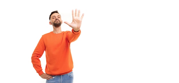 A man in an orange jumper on a white background stretches his palm forward with five fingers