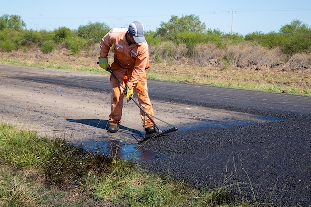 オレンジ色のジャンプ スーツを着た男性がシャベルを使って道路を掃除しています。