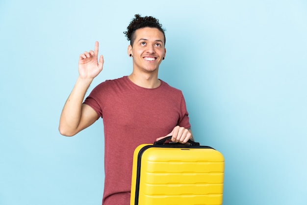 man over geïsoleerd blauw in vakantie met reiskoffer en omhoog