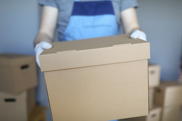 Man in overalls and gloves hold large cardboard box in his hand