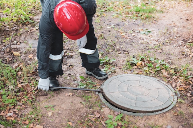 A man in overalls opens a sewer hatch cleaning of sewers and drains