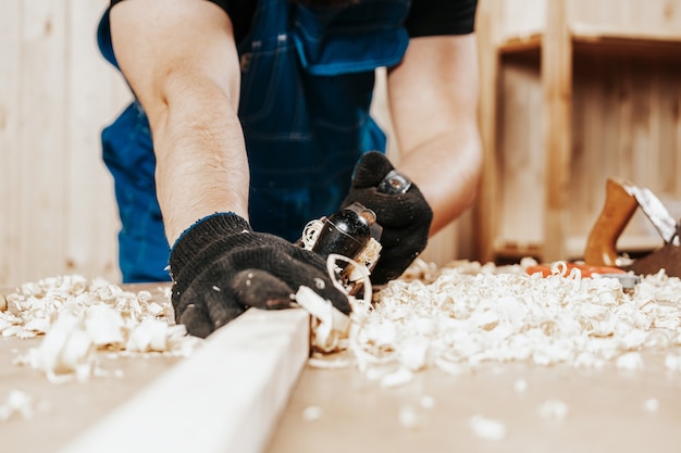 Man in overalls treating a wooden bar with a blackjack plane