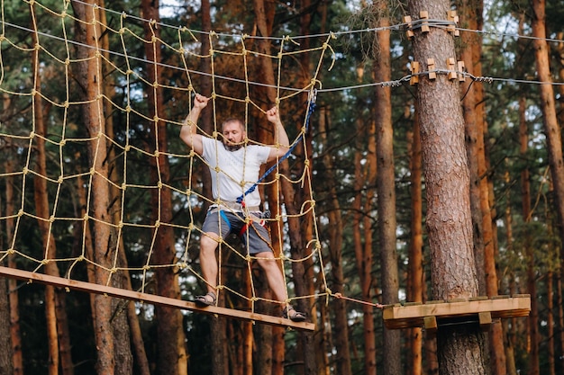 Un uomo supera un ostacolo in una città di corde un uomo in un parco avventura nella foresta