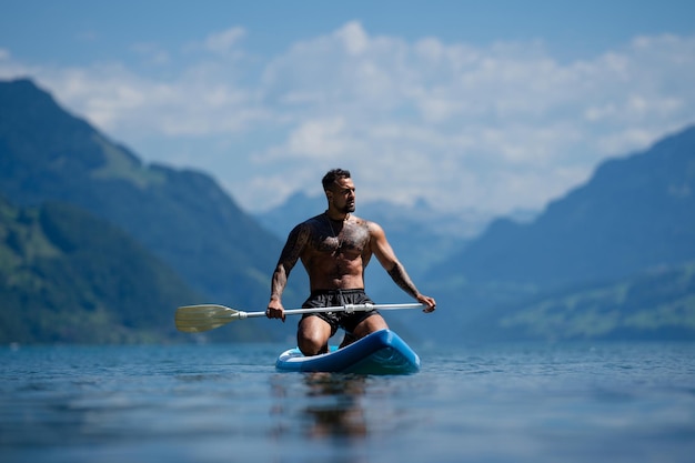 アルプスの湖山でペドルボードに乗る男 スイスの湖でペドルでレジャー活動する男