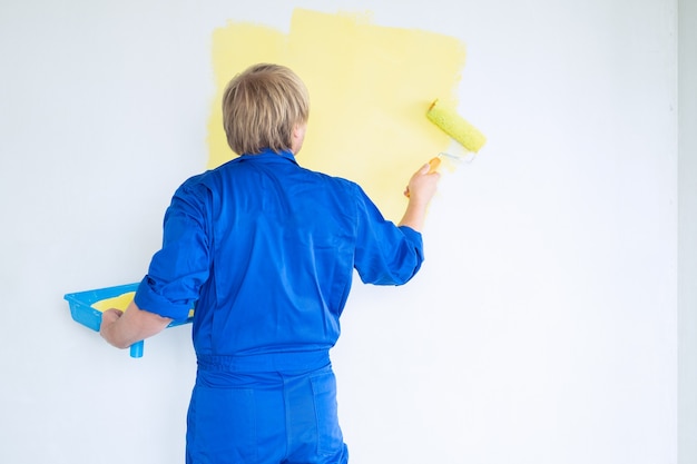 Man painting wall in yellow color with roller. Renovation, repair and redecoration concept.