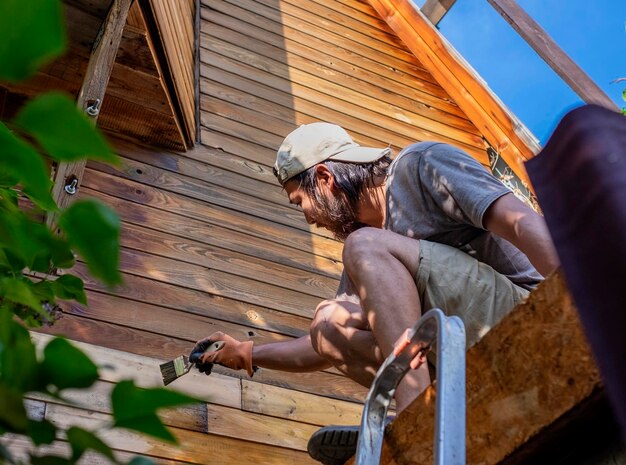 Мужчина красит деревянную стену дома на открытом воздухе
