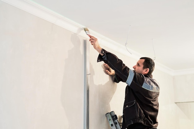 L'uomo dipinge un plinto del soffitto in gesso con un pennello riparazioni in corso nell'appartamento restauro all'interno pannello di cartongesso