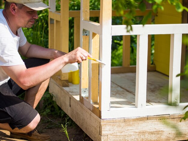 A man paints the terrace with a brush with white paint dad makes a children's house or hut for his daughter