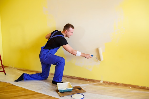 A man paints the wall in the house with a roller and paint. Renovation of rooms in the house.