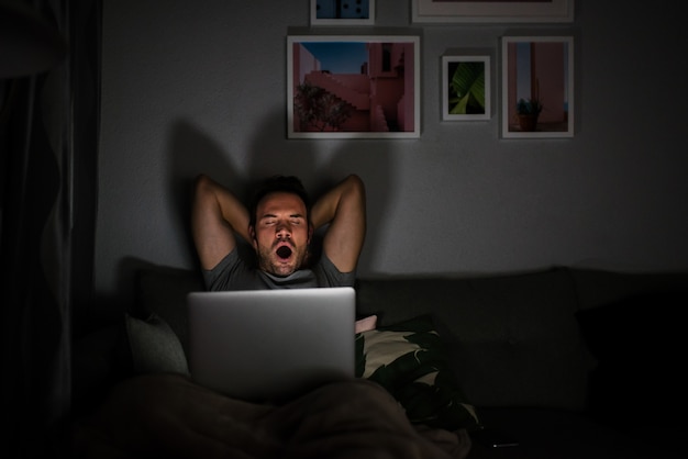 Man in pajamas with a computer yawning