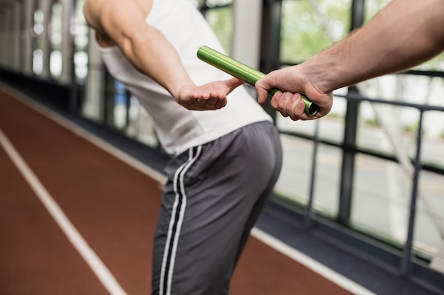 Uomo che passa il testimone al partner in pista in palestra