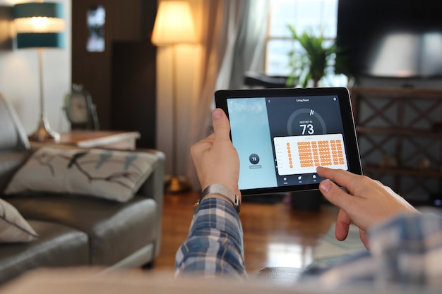 Man past een temperatuur aan met behulp van een tablet met smart home-app in moderne woonkamer