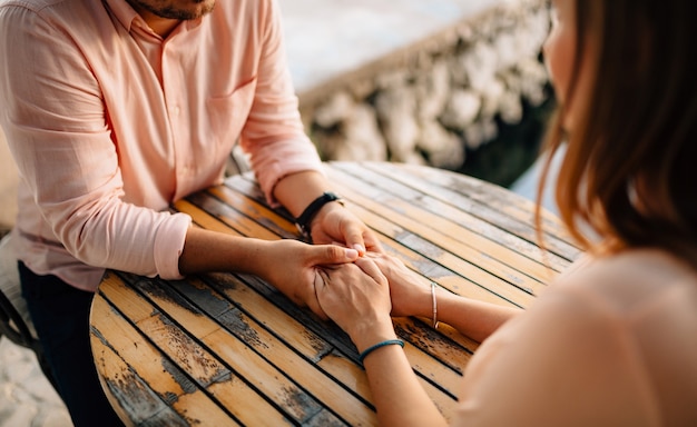 Man in a pastel shirt and a wristwatch holds the girls hands with bracelets behind a wooden table