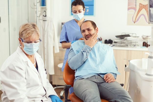 Пациент мужчина кладет руку на щеку, показывая зубную боль, жалуется на боль в зубах