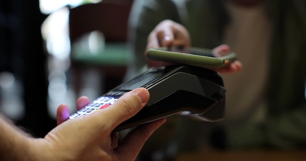 L'uomo paga tramite smartphone su macchina di pagamento elettronica o lettore di carte il cliente acquista l'ordine di cibo al caffè