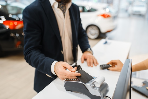 Man pays for the purchase of a new auto in car dealership. Customer and saleswoman in vehicle showroom, male person buying transport, automobile dealer business