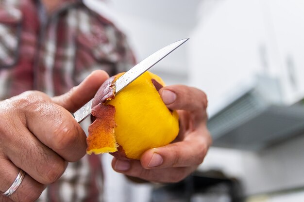 Man peeling a peach with a knife seen up close