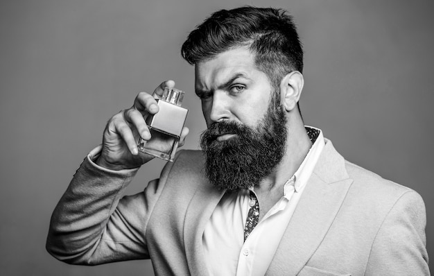 Man perfume, fragrance. Masculine perfume. Male fragrance and perfumery, cosmetics. Bearded man holding up bottle of perfume. Fashion cologne bottle. Bearded male prefers expensive fragrance smell.