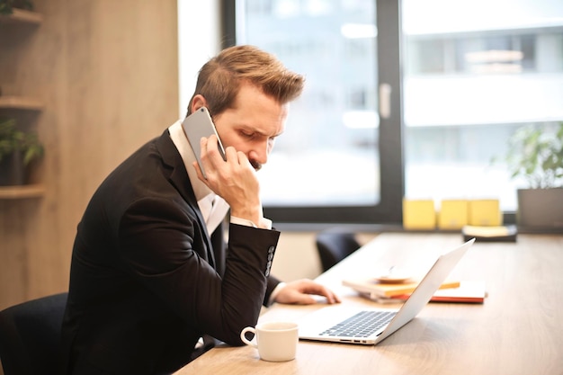 A man on a phone talks on a laptop.