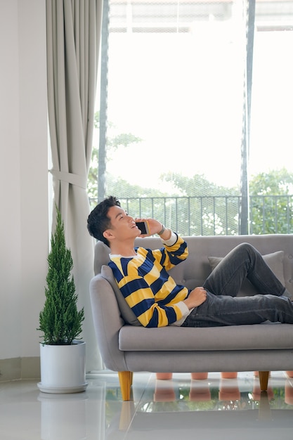 Man on the phone while sitting on his sofa against a white background