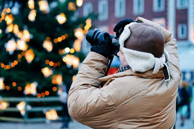 ラトビアの冬のリガのドーム広場のクリスマスツリーでカメラを持つ男の写真家。