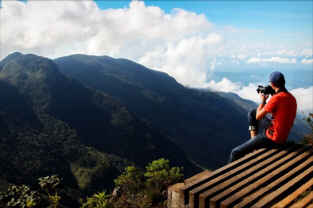 Мужчина фотографирует гору на краю обрыва Плато Конец Света Шри-Ланка