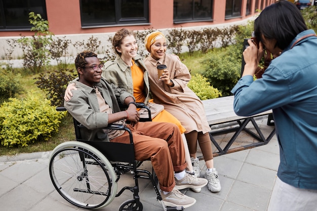 Uomo che fotografa un gruppo multietnico di amici, incluso un uomo disabile in sedia a rotelle all'aperto