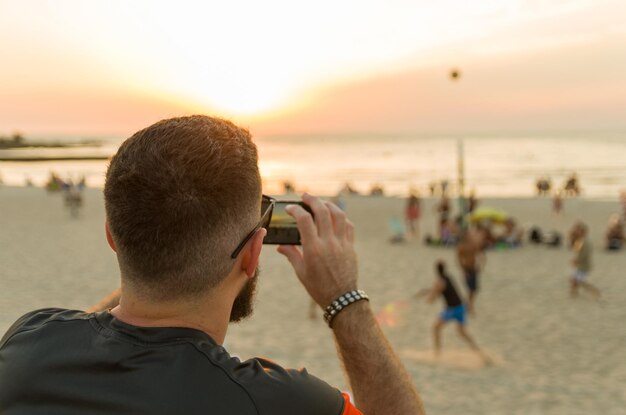 Man photographing sunset on the beach with smartphone