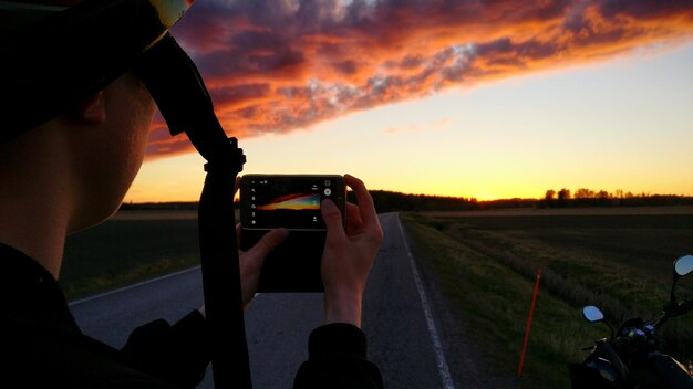 Photo man photographing sunset with mobile at footpath