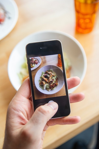 A man photographs a delicious salad on his phone in a restaurant