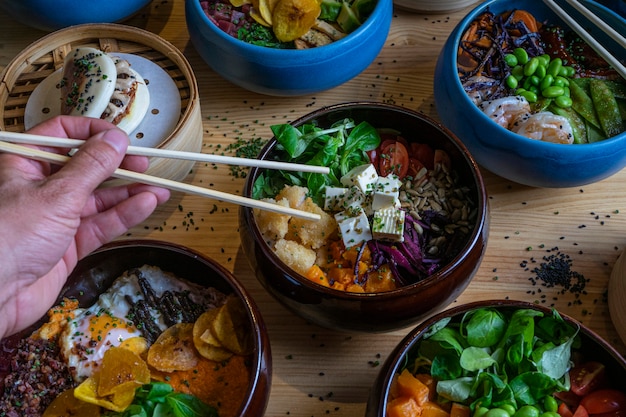 Man picking food by hand with chopsticks into the Poke Bowl on a wooden table.