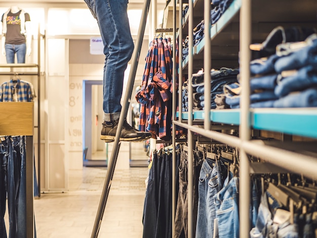 男は梯子の上の洋服店でジーンズを選ぶ