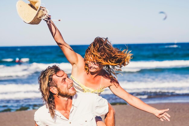 Man piggybacking cheerful woman at beach against sky