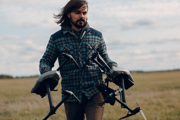 Man pilot holding quadcopter drone in hands at outside field.