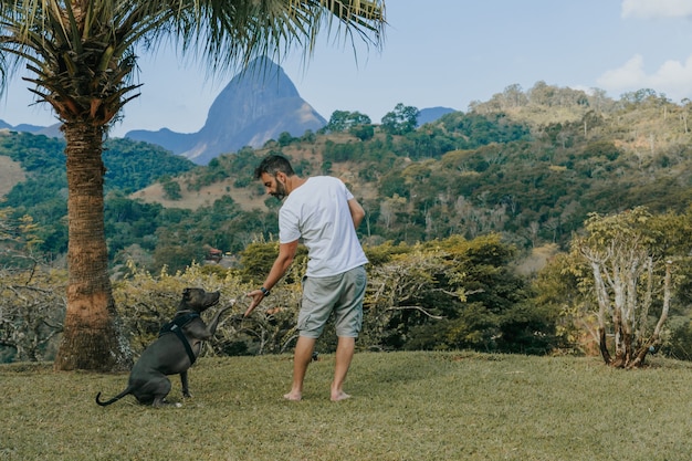 A man and a Pit Bull dog playing and admiring the nature and mountains of PetrÃ³polis, in Rio de Janeiro, Brazil. Affectionate relationship between human and animal.