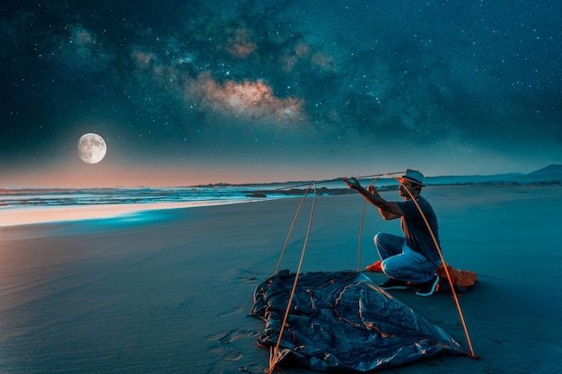 Man pitches a tent on the shore of the beach at nightxA