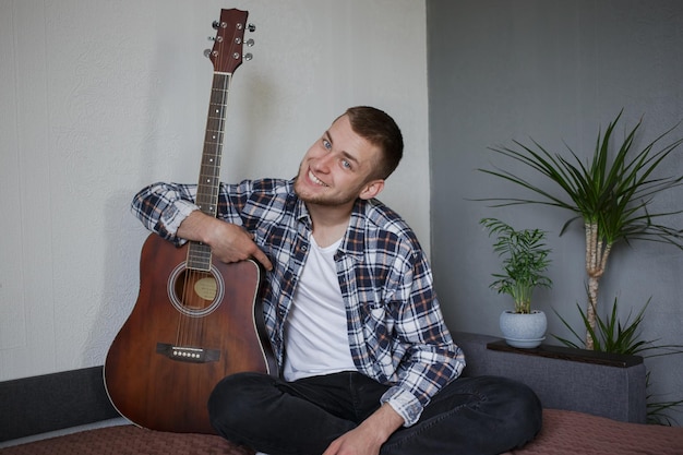 Мужчина в клетчатой рубашке обнимает свою гитару и улыбается