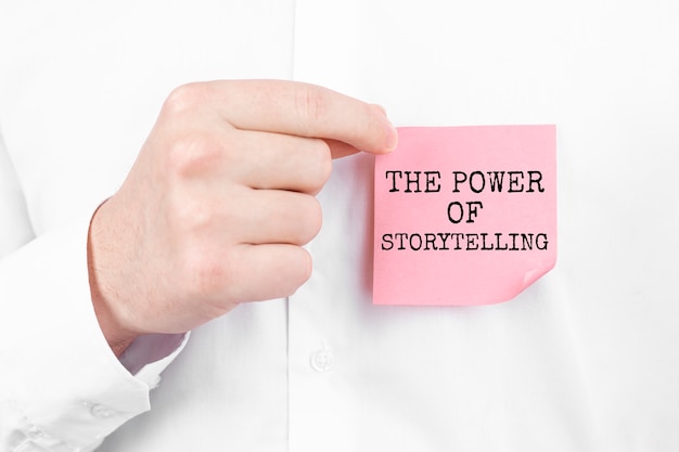 Man plakt een rode sticker met de tekst The power of Storytelling overlay op zijn witte overhemd