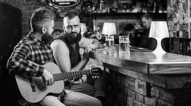 Man play guitar in bar Cheerful friends relax with guitar music Friday relaxation in bar Friends relaxing in bar or pub Real men leisure Hipster brutal bearded spend leisure with friend in bar