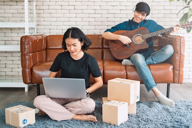 Man playing acoustic guitar with woman using laptop on sofa in living room