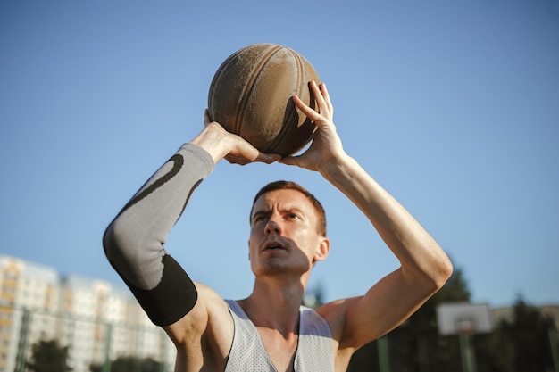 Uomo che gioca a basket e lancia palla nel parco giochi urbano