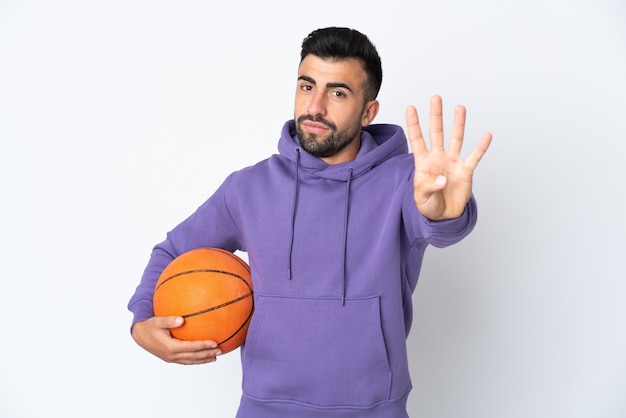 Человек играет в баскетбол над белой стеной счастлив и считает четыре пальцами