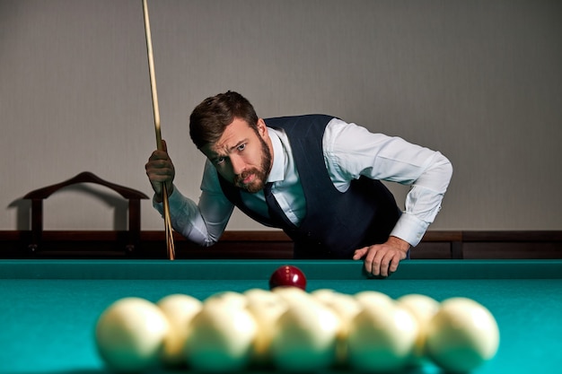 Man playing billiard or snooker with concentration and serious face looking at balls on table, sport game concept