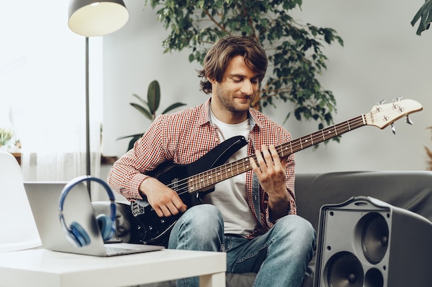man playing electric guitar and recording music into laptop