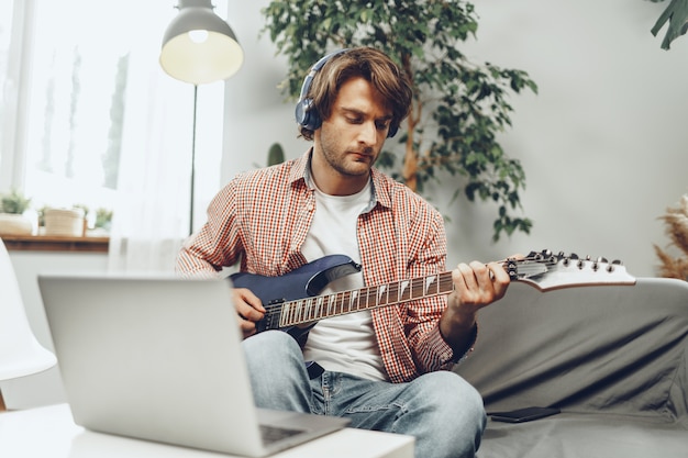 man playing electric guitar and recording music into laptop