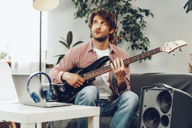 man playing electric guitar and recording music into laptop