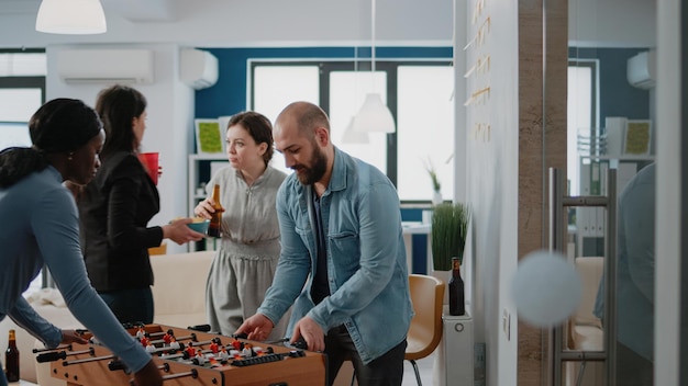 Man playing foosball game at table with woman and losing, having drinks after work. Colleagues meeting to drink beer and have fun with football game, enjoying free time after hours