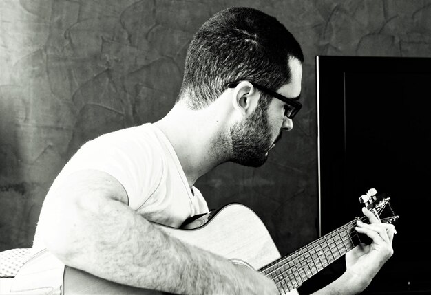 Photo man playing guitar against wall at home