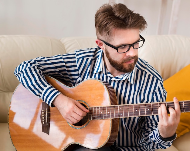 写真 自宅のソファーでギターを弾く男