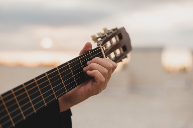 Foto uomo che suona la chitarra sul tetto sullo sfondo del tramonto